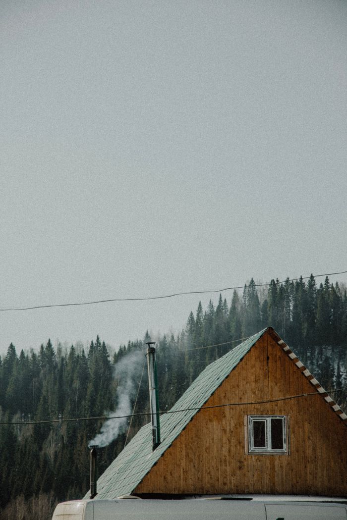 A cozy wooden house with smoke from the chimney, nestled in a snowy forest setting in Ust'-Koiva, Russia.