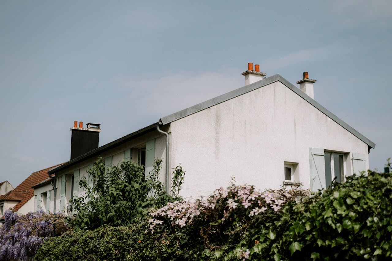 Rustic cottage with a pitched roof and blooming flowers against a clear sky.