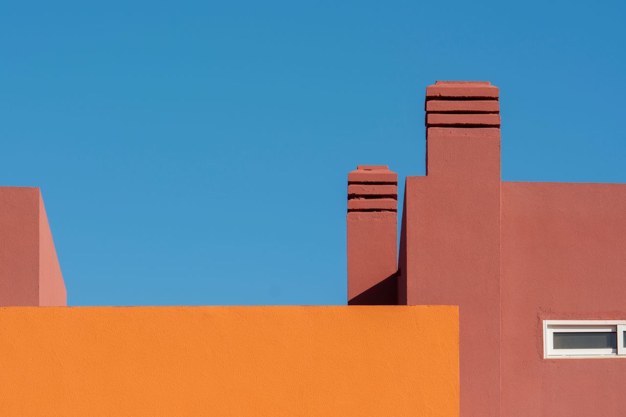 Bright orange and red building facade with blue sky backdrop, minimalistic modern design.