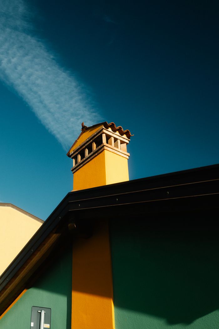 Vibrant yellow and green building rooftop with chimney against a clear blue sky, showcasing colorful architecture.